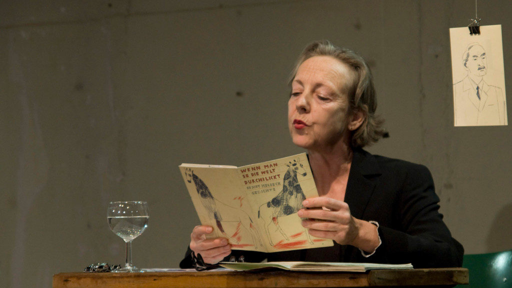Scene photo of a performance: One woman is reading a newspaper on a stage.