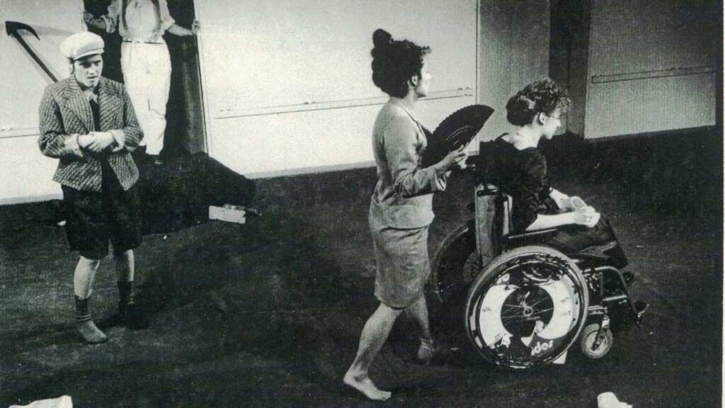 Scene photo of a performance: Four people on a stage. One in a wheelchair.