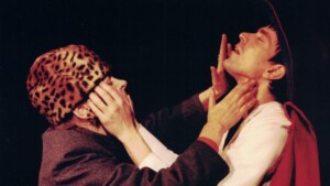 Szenenfoto aus einer Auffuehrung: Eine Frau mit Tigerfellkappe und ein Mann berühren gegenseitig ihre Gesichter.n