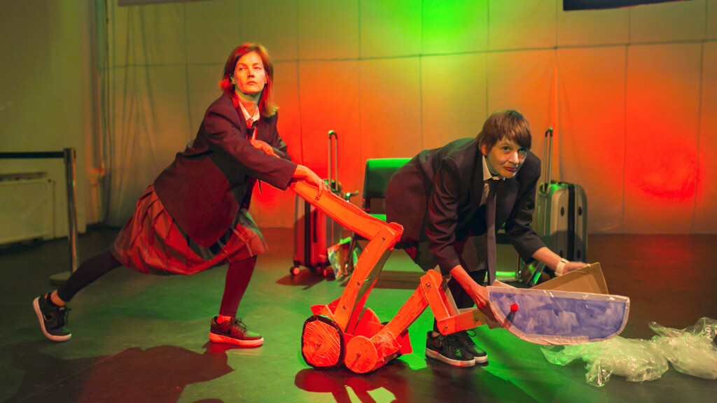 Scene photo of a performance: Two women on a stage pushing a digger.