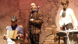 Szenenfoto aus einer Auffuehrung: Drei Maenner in historischen Kostuemen hinter einem Mikrofon. Einer traegt ein Waldhorn