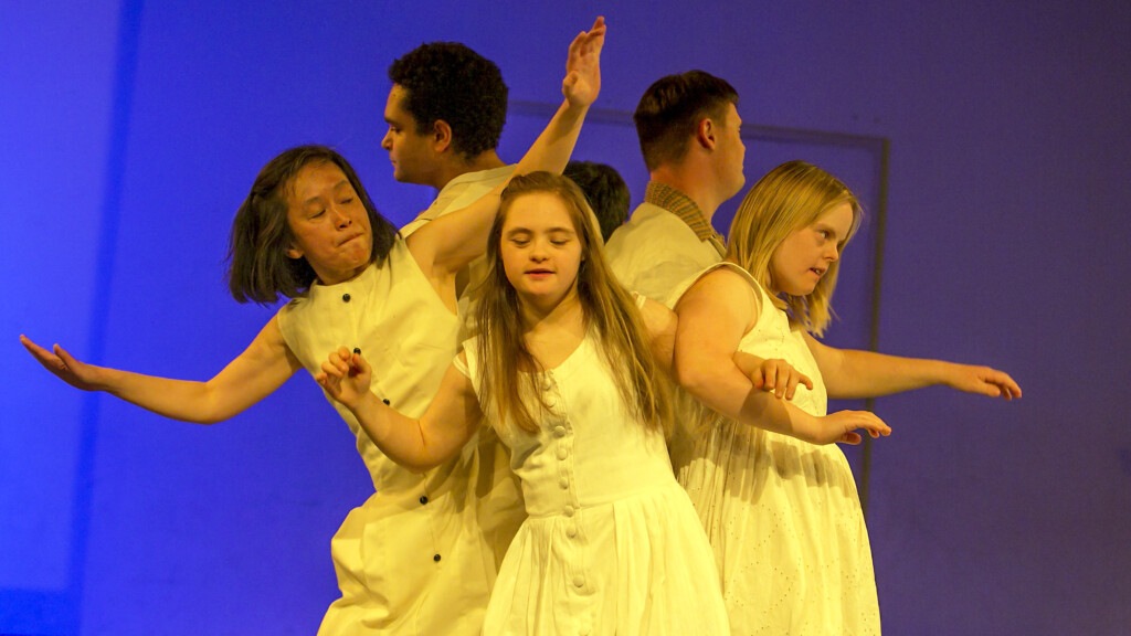 A group of dancers wearing white clothes in front of a blue background.