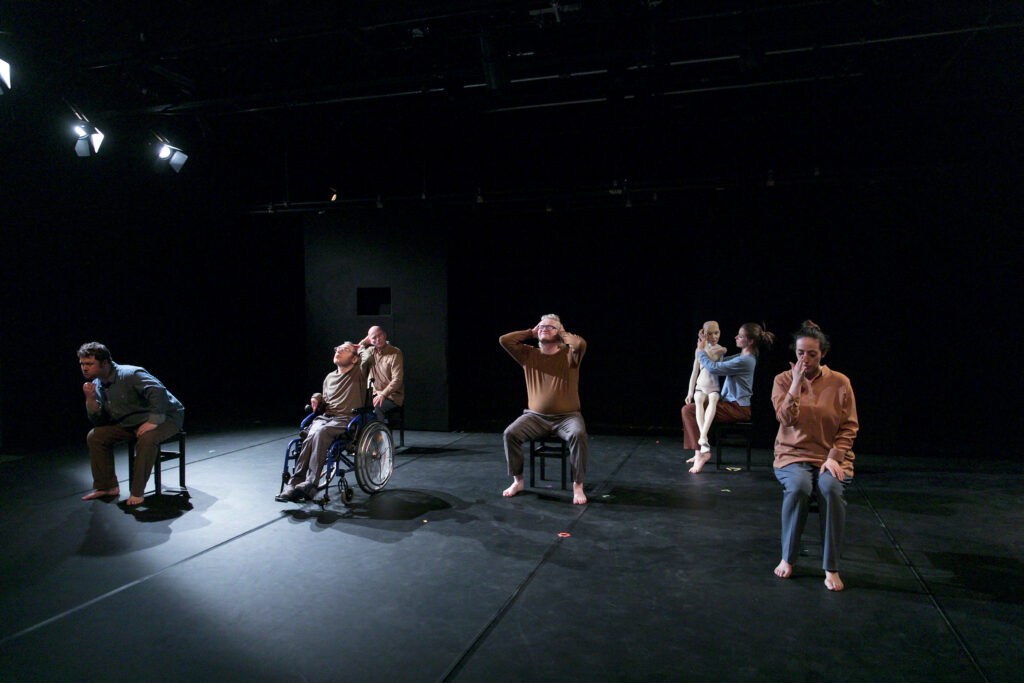 Scene photo of a performance: A couple people are sitting on small chairs on a stage.